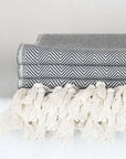 Close-up side image of a grey colour blanket with knotted fringe style.